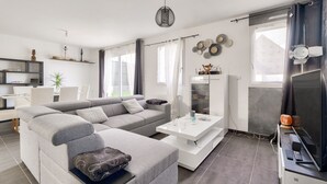 A modern living room with a grey sectional sofa, a white coffee table, and a flat-screen TV. - New and cozy house for 6 with garden (Beaussais-Sur-Mer)