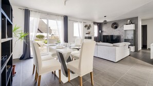 A modern living room with a sofa, a dining table with chairs, and a fireplace. - New and cozy house for 6 with garden (Beaussais-Sur-Mer)