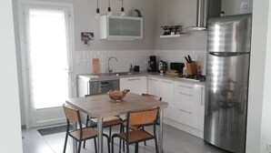 A modern kitchen with a stainless steel refrigerator, white cabinets, and a wooden dining table with chairs. - Detached house with garden, close to the sea. (Saint-Hilaire-de-Riez)