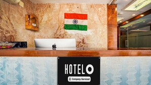 A hotel reception desk with a marble wall, an Indian flag, and a sign indicating it's a company-serviced hotel.