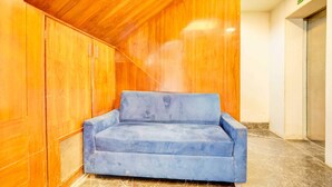 A blue sofa in a corner with wooden paneling and a marble floor.