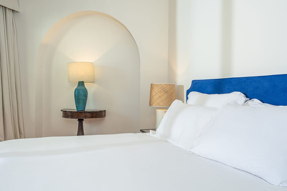 A hotel room with a bed, two bedside tables, a lamp, and a wall arch.
