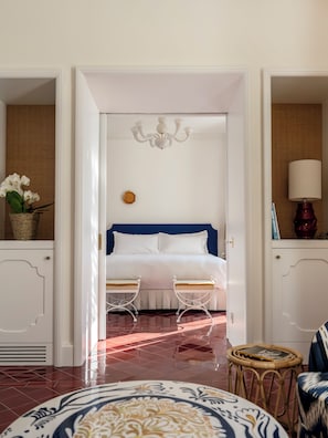 Un dormitorio con una cama, dos mesitas de noche, una araña y una cesta de mimbre con flores.
