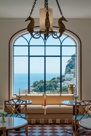 Ein Zimmer mit einem großen Bogenfenster, einer Kristallleuchter, einer Couch und einem Esstisch.