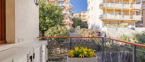 Un balcón con una planta en maceta, piso de baldosas y vista a edificios de varios pisos.