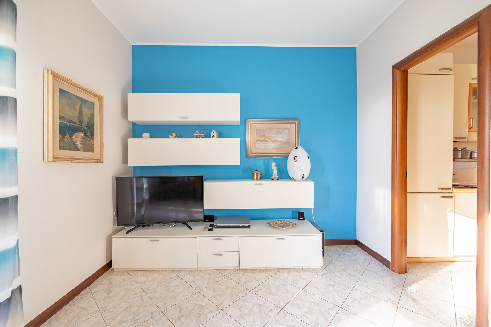 Ein modernes Wohnzimmer mit blauer Akzentwand, einem Flachbildfernseher, einer weißen Unterhaltungseinheit und einer Tür zu einem anderen Raum.