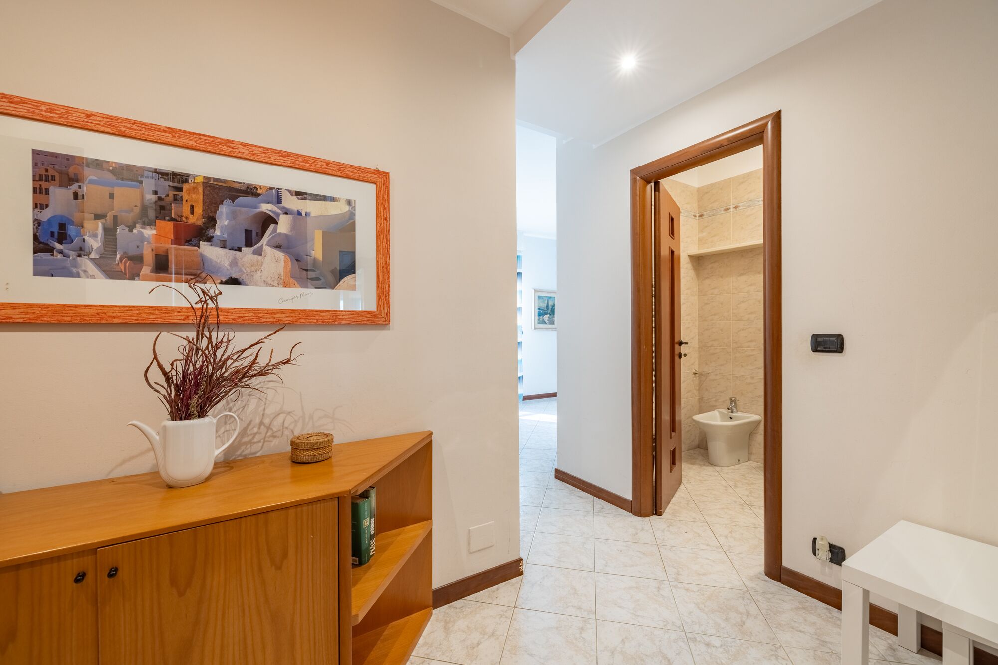 A hallway with a wooden console table, a framed picture, and a bathroom visible through an open door.