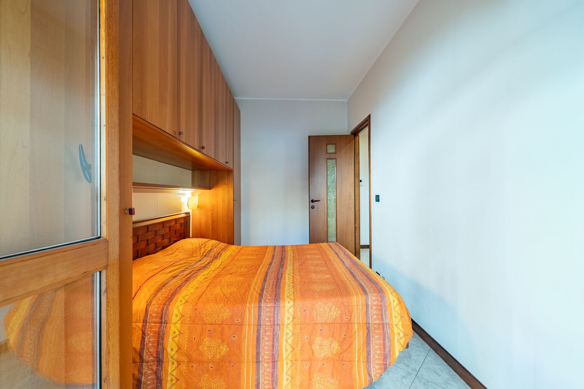 Ein schmaler Flur mit einem Bett am Ende, Holzschränken und einer Tür mit Verzierungen.