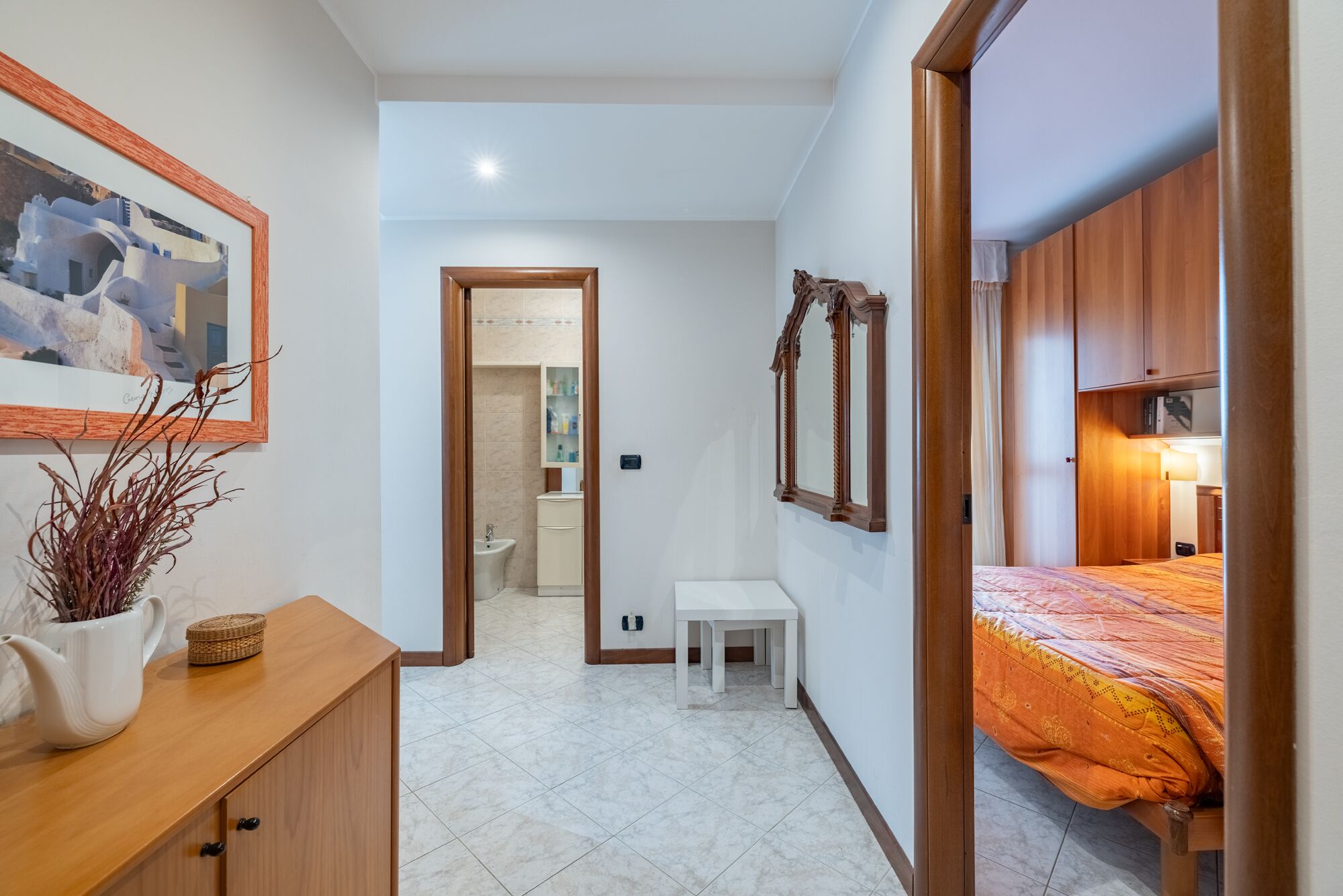 A bedroom with a bed, a bedside table, a mirror, and a wooden wardrobe.