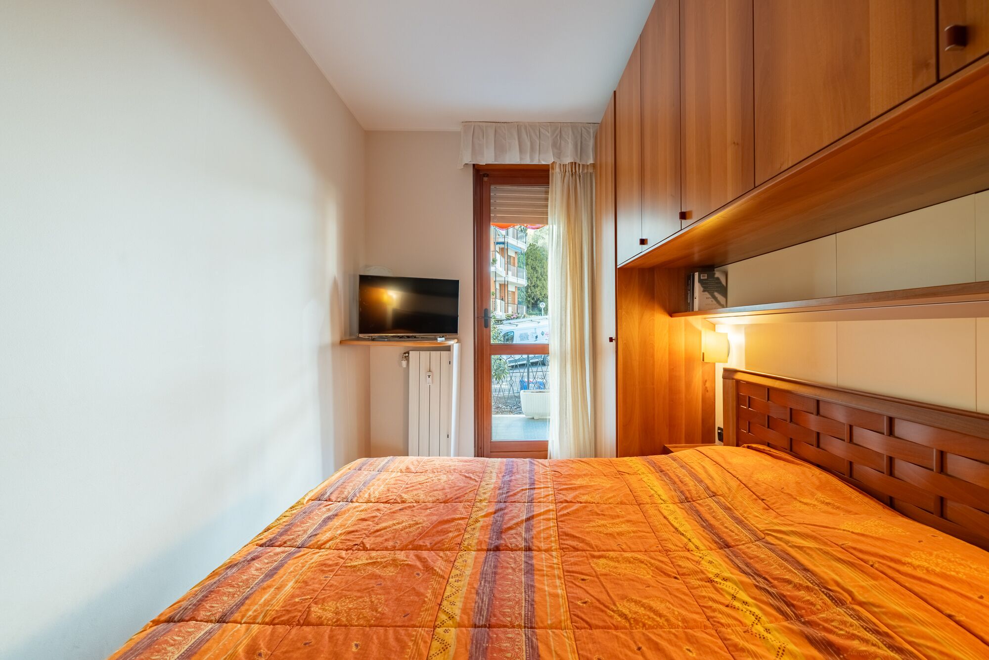 A bedroom with a bed, wooden wardrobe, and a television on a shelf.