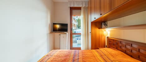 A bedroom with a bed, wooden wardrobe, and a television on a shelf.
