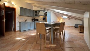 A kitchen with a dining area, featuring a wooden ceiling, tiled floor, and a small dining table with chairs. - Attic 8 (Nago-Torbole)