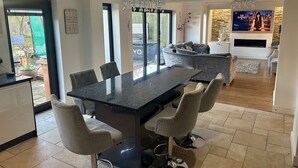 A modern kitchen with a central island, bar stools, and a dining table. - Luxury 5 Bedroom Group House near Cardiff with Sauna and Games Lounge (Penarth)