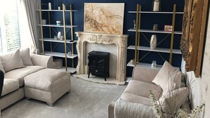 A living room with a fireplace, beige sofas, a chandelier, and decorative shelves. - Luxury 5 Bedroom Group House near Cardiff with Sauna and Games Lounge (Penarth)