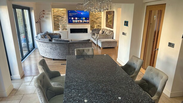 A modern living room with a sectional sofa, a dining table with chairs, and a flat-screen TV mounted on the wall. - Luxury 5 Bedroom Group House near Cardiff with Sauna and Games Lounge (Penarth)