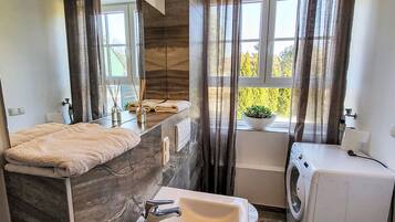 Une salle de bain moderne avec un comptoir en marbre, un lavabo, un lave-linge et une fenêtre donnant sur un paysage verdoyant.