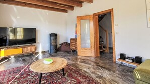Un ampio soggiorno con soffitto in legno, televisione a schermo piatto, stufa a legna, un tavolo rotondo in legno e un tappeto decorato.