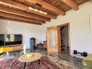 A spacious living room with a wooden ceiling, a flat-screen TV, a wood-burning stove, a round wooden table, and a patterned rug. - Kallinchen am Motzener See by Interhome (Mittenwalde)