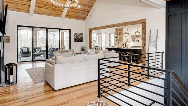 A spacious living area with a white sofa, wooden flooring, and a large window.