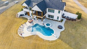 A two-story house with a large backyard featuring a swimming pool, outdoor seating, and a hot tub.