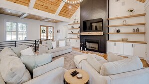 A spacious living room with a fireplace, white sofas, and wooden shelves.