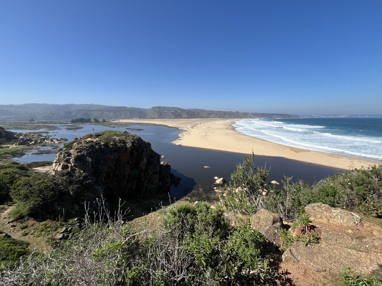 Un paysage côtier avec une plage, des affleurements rocheux et un ciel bleu dégagé.