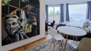A modern living room with a large abstract painting, a round dining table, and a view of the ocean. - Oceanfront Apartment Estudio el Suspiro (Tunquen)