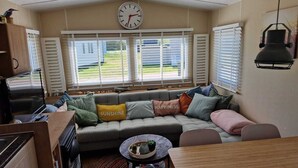 A cozy living area with a sofa, a round coffee table, and a clock on the wall. - 2 minutes from the beach! Mobile home Duingras Ameland (Nes)