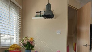 A dining area with a wooden table, two white chairs, a hanging light fixture, and a window with blinds. - 2 minutes from the beach! Mobile home Duingras Ameland (Nes)