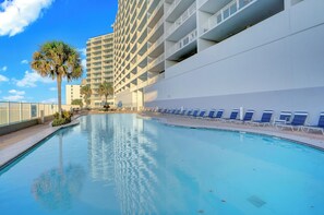 A swimming pool with lounge chairs, a palm tree, and a tall building in the background. - Lighthouse 1215 by Liquid Life (Gulf Shores)