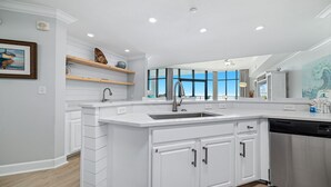 Een moderne keuken met witte kastjes, een groot eiland met een spoelbak en uitzicht op buiten.