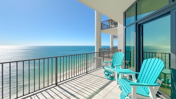 Een balkon met turquoise Adirondack-stoelen met uitzicht op een heldere blauwe oceaan.