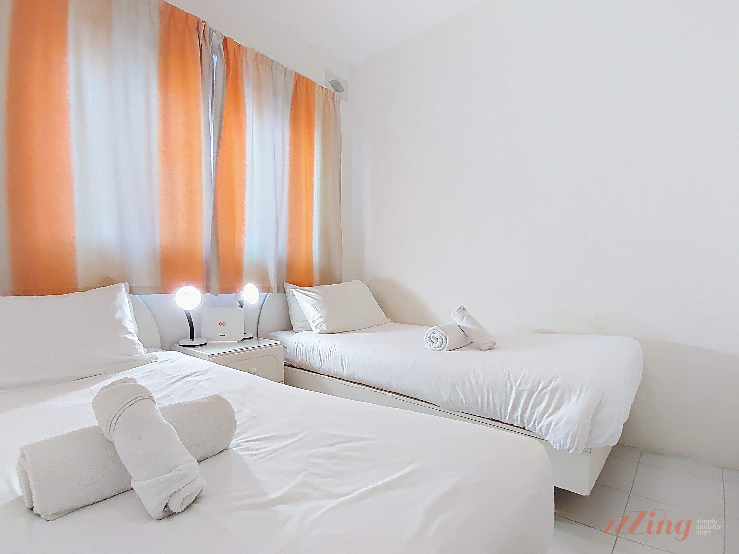 A hotel room with two beds, a vanity with lights, and a curtain with orange and white stripes.