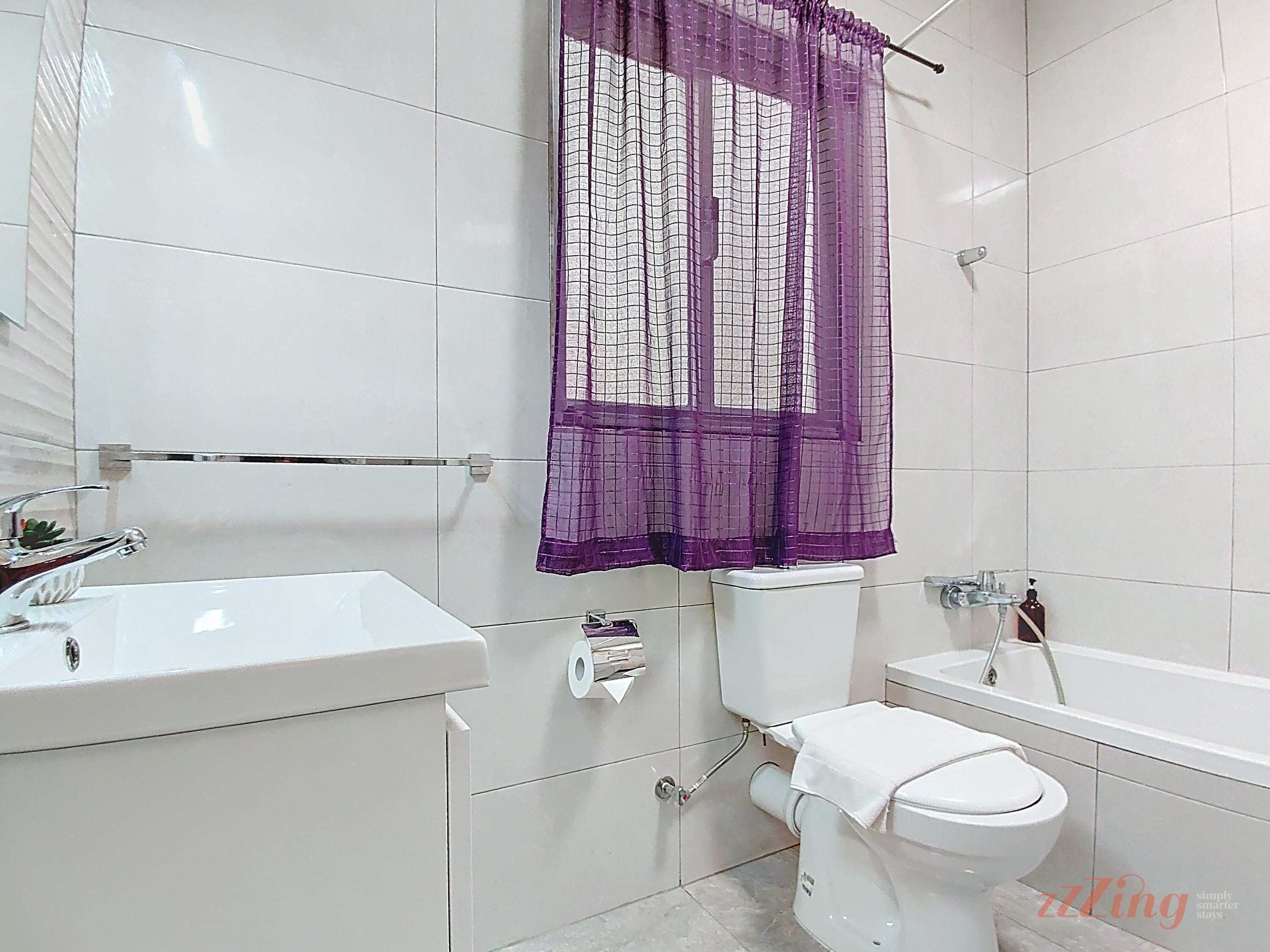 Un baño con paredes de azulejos blancos, un lavabo blanco, un inodoro y una bañera.