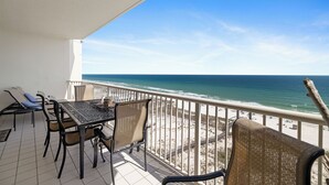 Un balcon avec une table et des chaises, donnant sur une plage et l’océan.