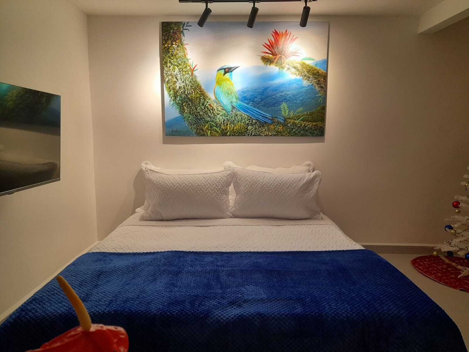 A bedroom with a bed, white pillows, a blue blanket, and a wall-mounted painting of birds.