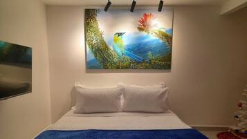 A bedroom with a bed, white pillows, a blue blanket, and a wall-mounted painting of birds.