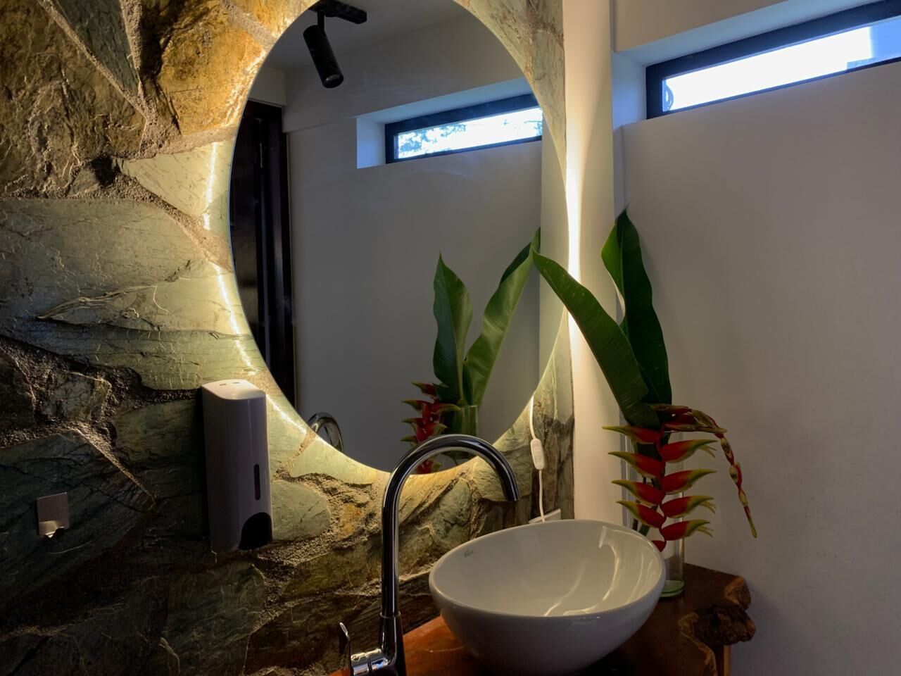 A bathroom with a stone wall, a modern sink, and a large mirror.