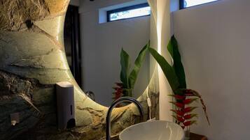 A bathroom with a stone wall, a modern sink, and a large mirror.