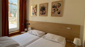 A hotel room with two beds, a window with curtains, and three framed botanical prints on the wall. - Baia Terrazza 1 (Nago-Torbole)