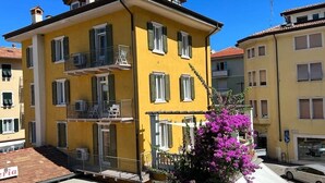 A yellow multi-story building with balconies, a visible sign reading "Hotel," and a purple flowering plant in the foreground. - Baia Terrazza 1 (Nago-Torbole)