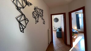 A hallway with geometric wall art, a clock, and a view into a living room with a blue sofa and a plant. - Baia Terrazza 1 (Nago-Torbole)