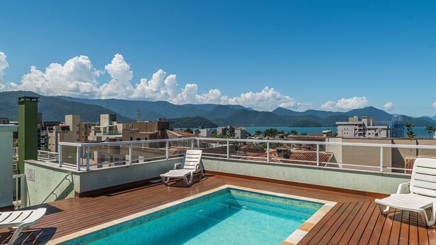 A rooftop pool with lounge chairs, a view of mountains, and a cityscape in the background. - Apt in Condo w/ Pool 350m From the Beach Pvj0021 (Ubatuba)