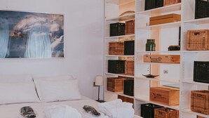 A hotel room with a neatly made bed, a wall-mounted painting, and shelves with baskets and boxes. - Family Apartment City Center - Mirable PM (Milano)