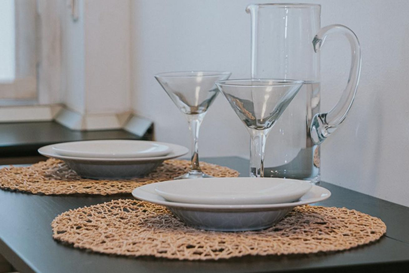 A table with two plates, a pitcher, and two glasses on a tablecloth.