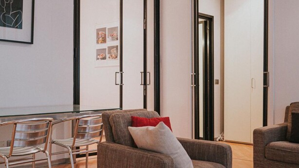 A modern living room with a glass dining table, metal chairs, and a sofa with cushions. - Family Apartment City Center - Mirable PM (Milano)