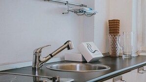A modern kitchen with a stainless steel sink, a faucet, and a soap dispenser. There is a glass container and a metal basket on the counter. - Family Apartment City Center - Mirable PM (Milano)