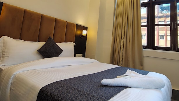 Une chambre d’hôtel avec un grand lit, un ventilateur de plafond, une fenêtre avec des rideaux et une vue sur les bâtiments environnants.