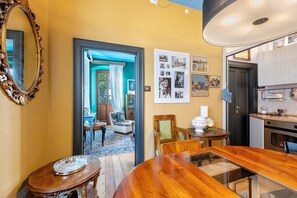 Un comedor con mesa de madera, sillas y un espejo. Se ve una cocina a través de una puerta abierta.