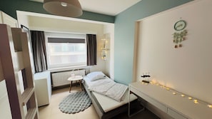 A compact bedroom with a bed, bedside table, and a window with curtains. - Luxury apartment with spacious terrace, frontal sea view 4 to 5 people (Blankenberge)
